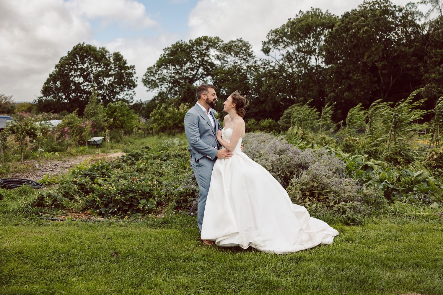 A romantic wedding couple embraces in a lush green garden setting during their outdoor photo session.