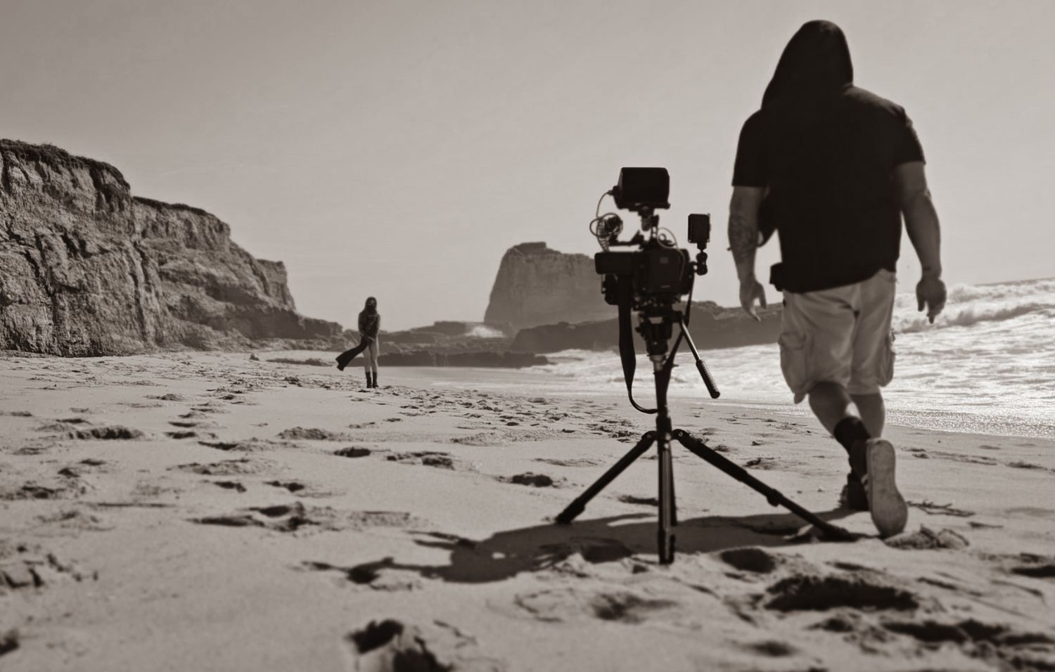 A series of black and white photographs showing a photographer setting up camera equipment on a sandy beach.