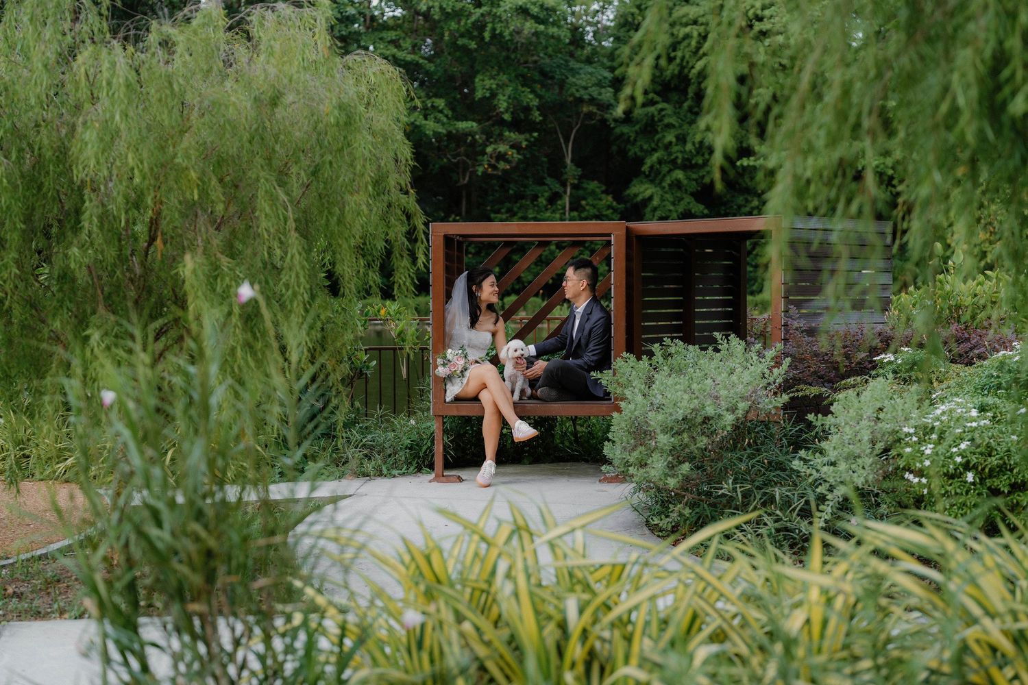Wooden garden pergola surrounded by lush greenery and flowering plants along a curved pathway.