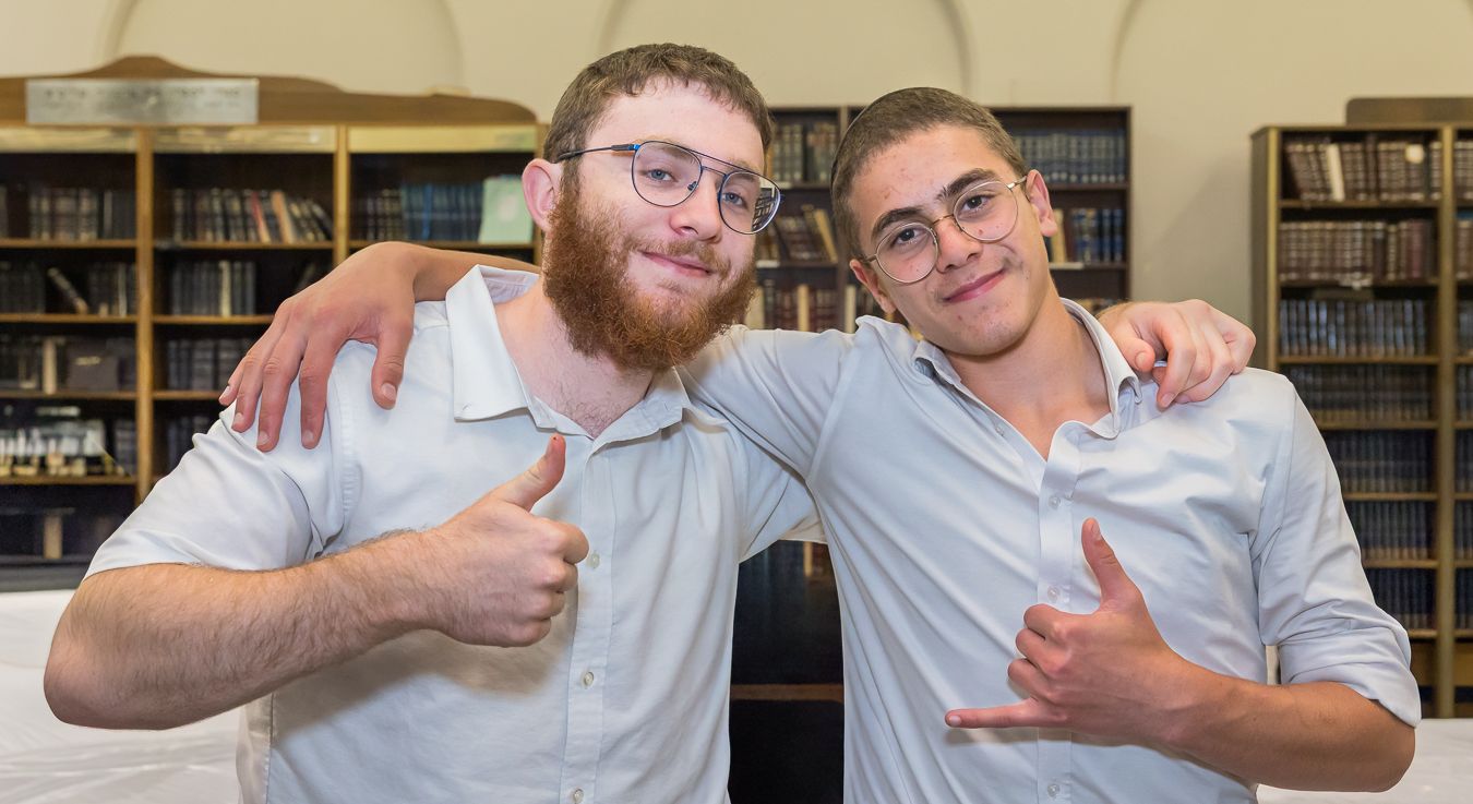 Two people posing together in front of library bookshelves while giving thumbs up gestures.
