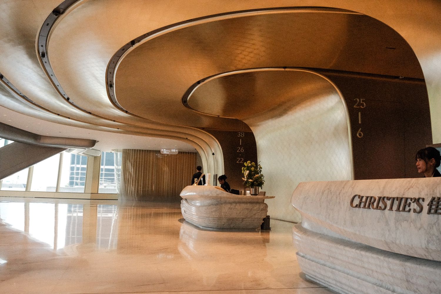 Christie's auction house lobby featuring sweeping curved architecture with golden walls and a marble reception desk.