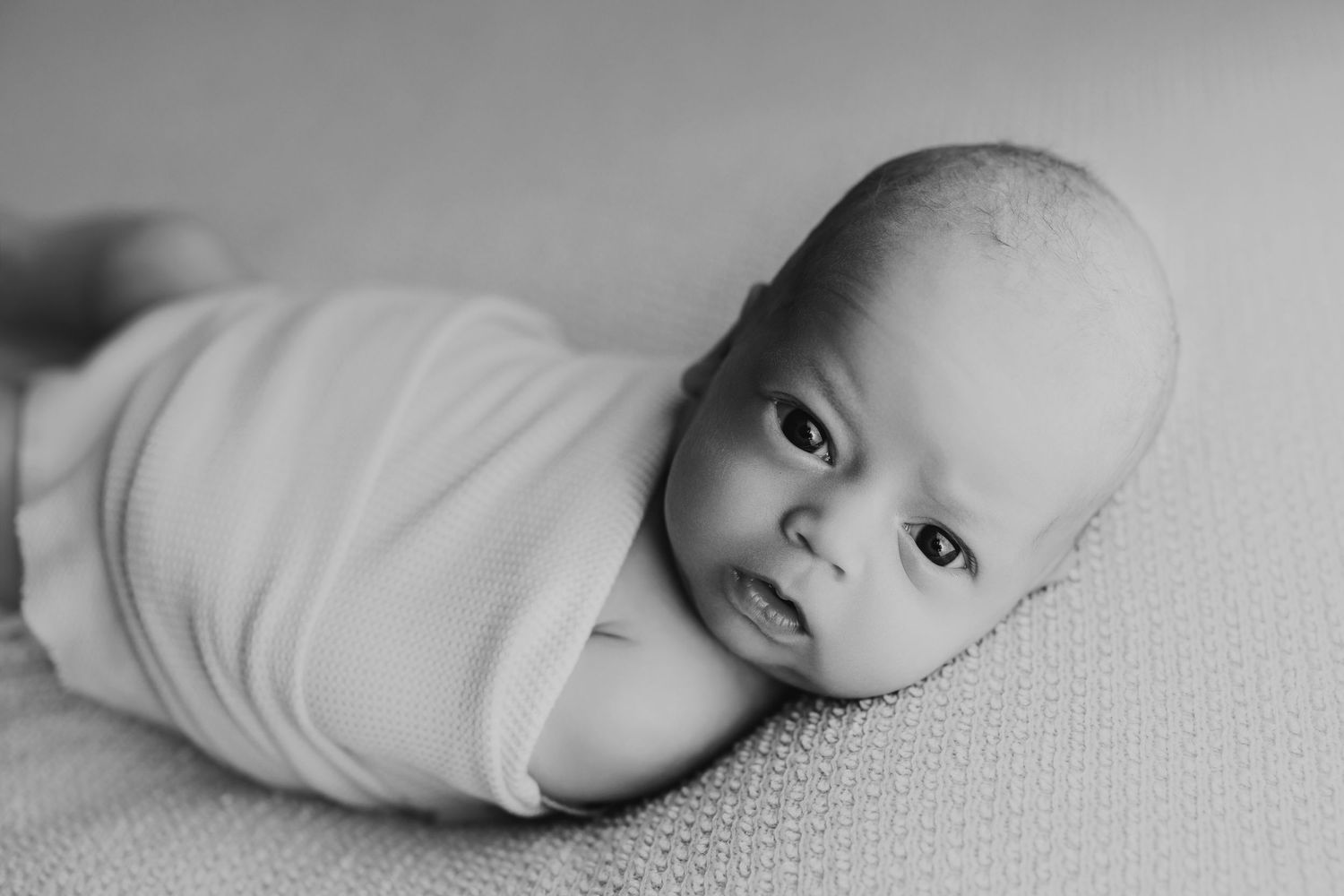 Black and white portrait of a newborn baby laying on soft textured fabric in a side-lying position.