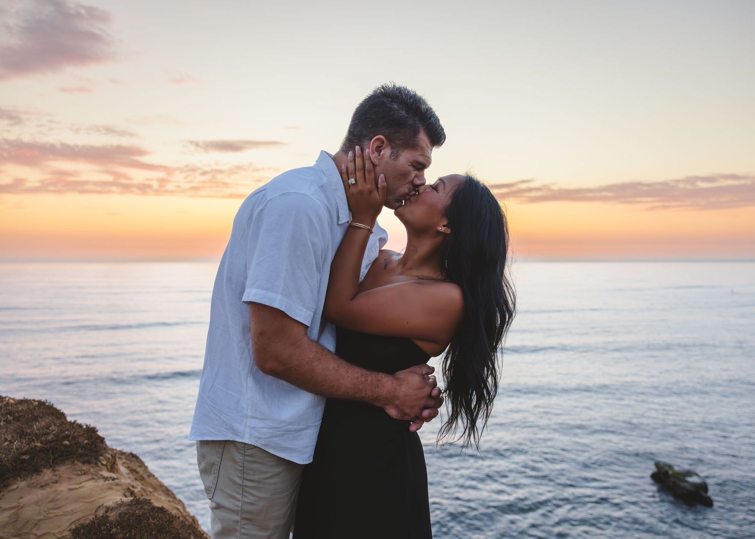 Couple sharing passionate moment on oceanside cliff during sunset.