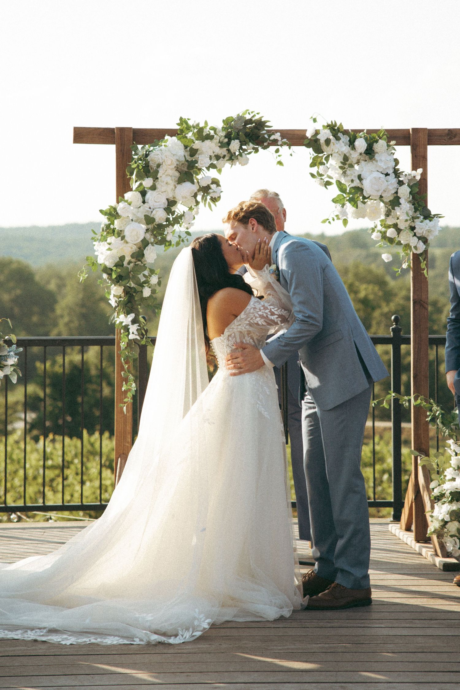 Newlyweds share their first kiss under a beautiful floral arch during an outdoor mountain wedding ceremony.