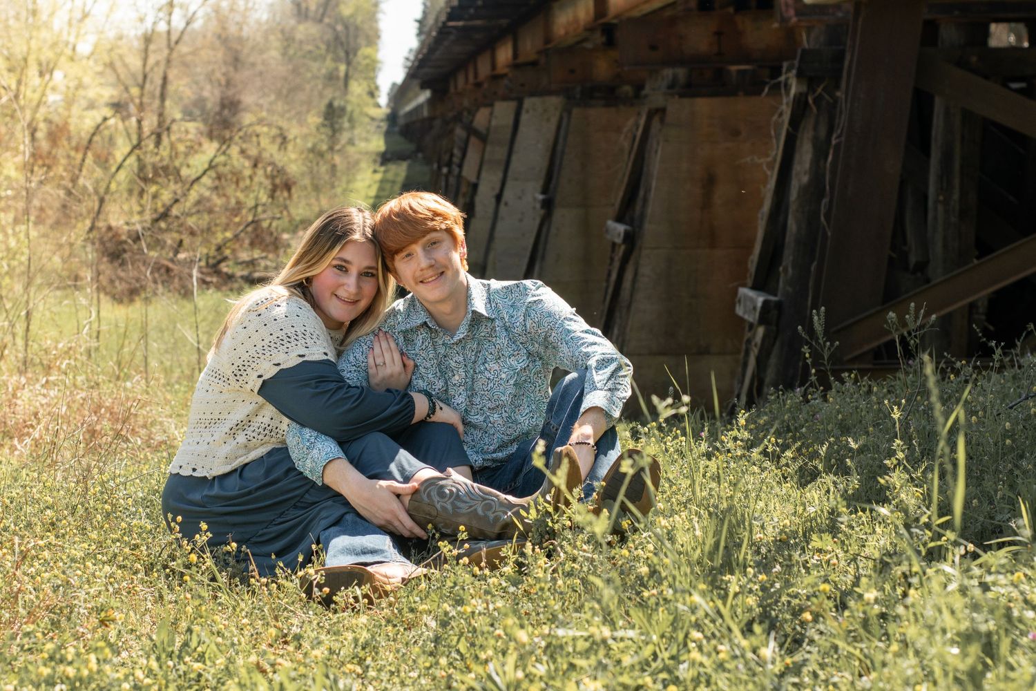 Nostalgic couple sitting in grass meadow near rustic wooden barn on a sunny day.