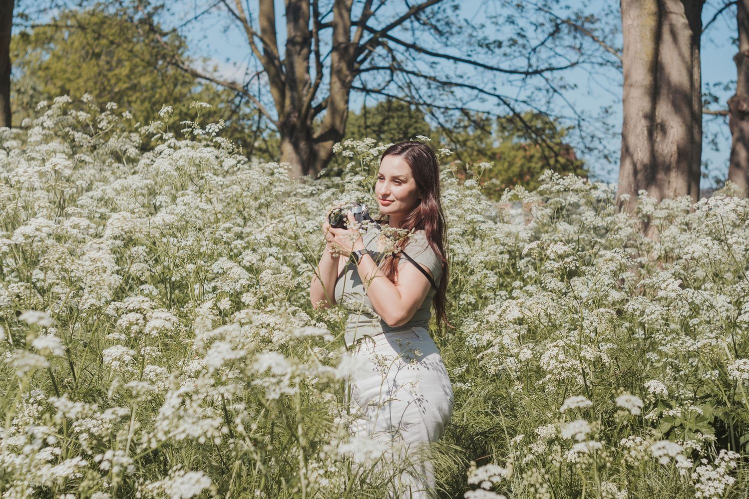 Photographer Abelim stands among blooming white wildflowers in a sunlit wooded area on a summer day.