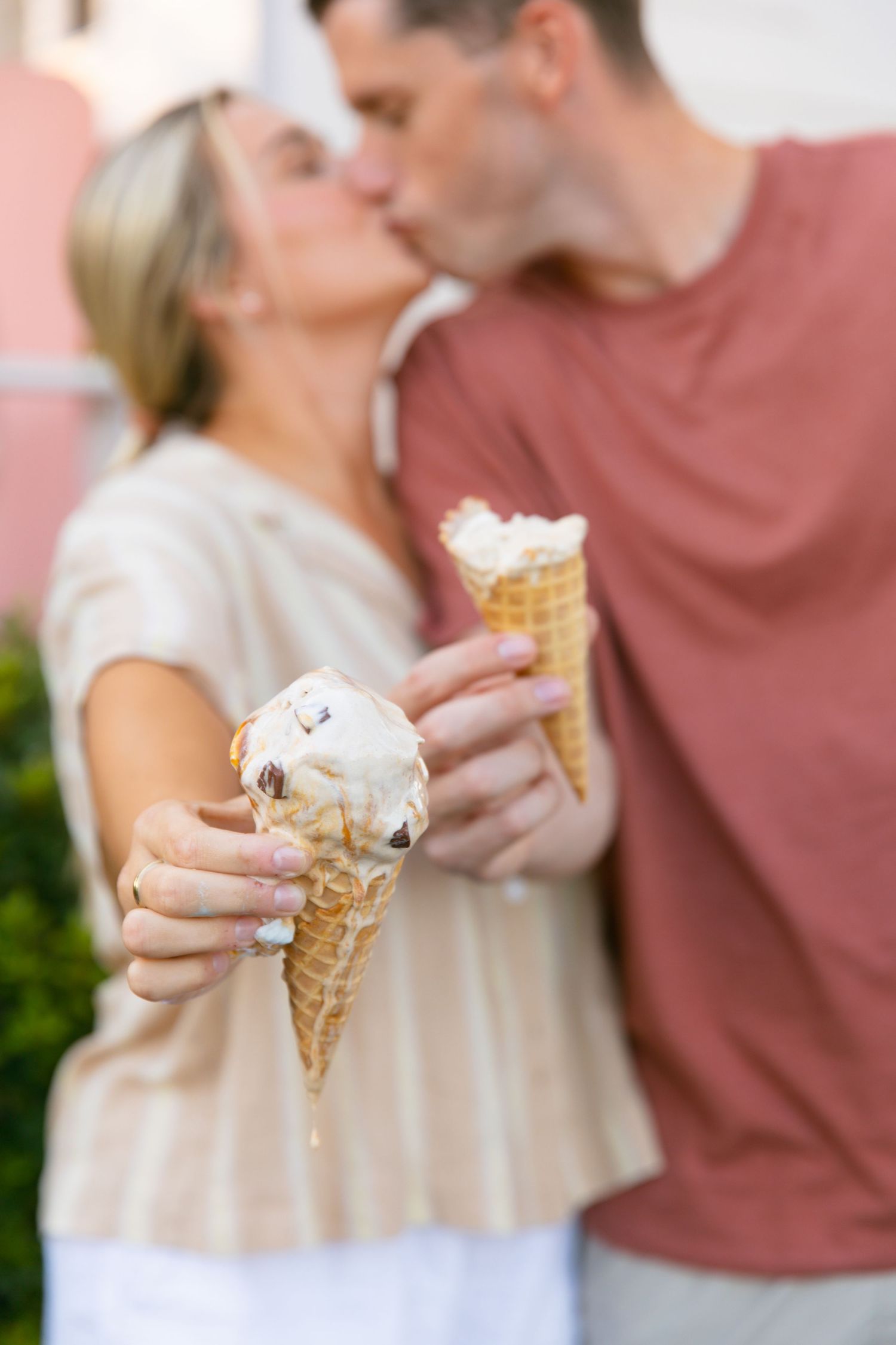 Romantic couple sharing ice cream cones and a kiss outside a pink-colored building.
