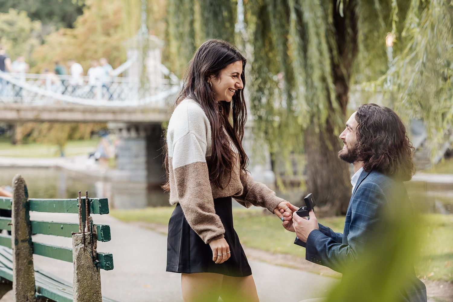 Romantic marriage proposal scene by bridge with willow trees in background.