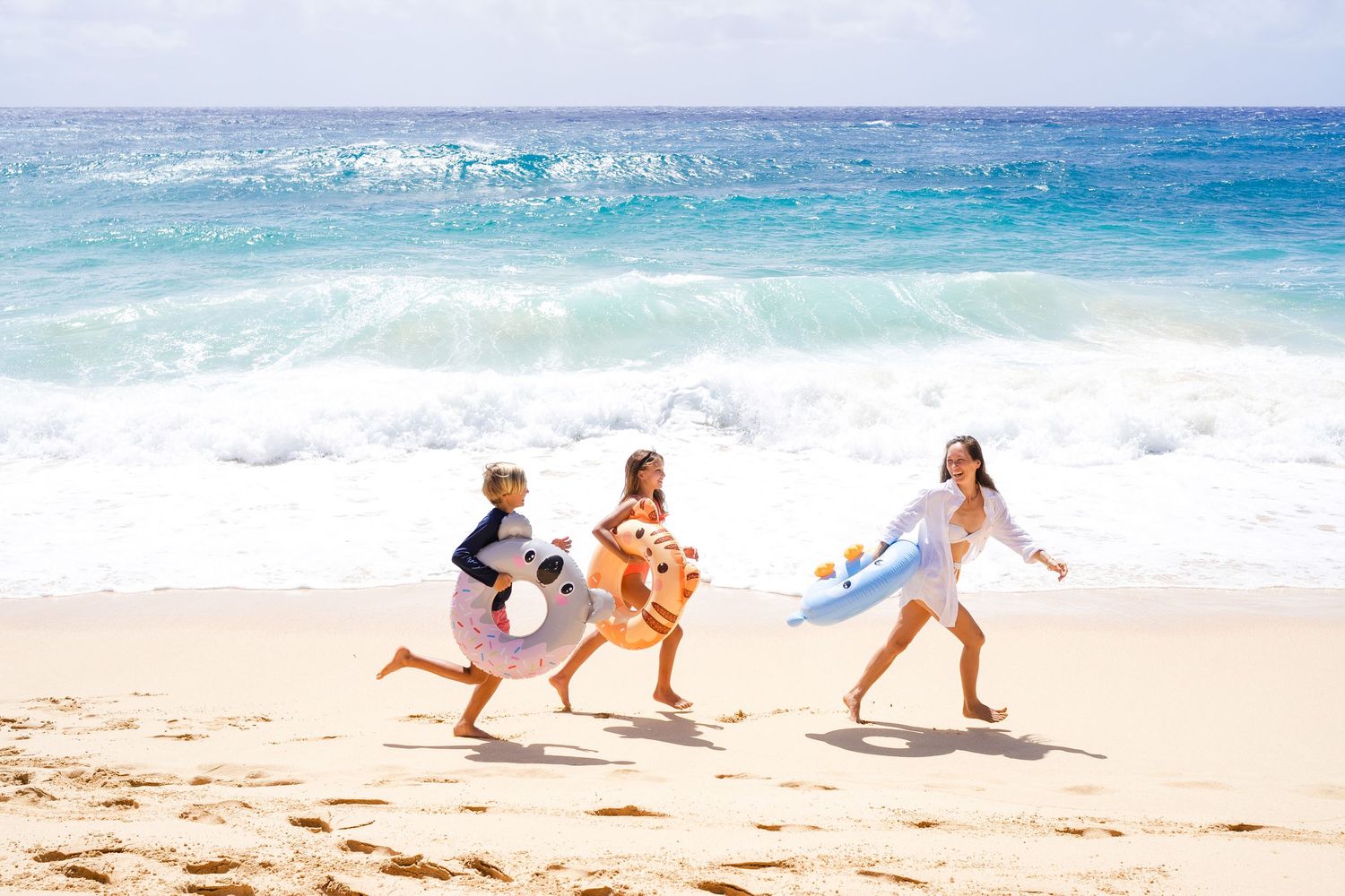 Three people running and playing joyfully along a tropical beach with turquoise waves crashing on the shore.