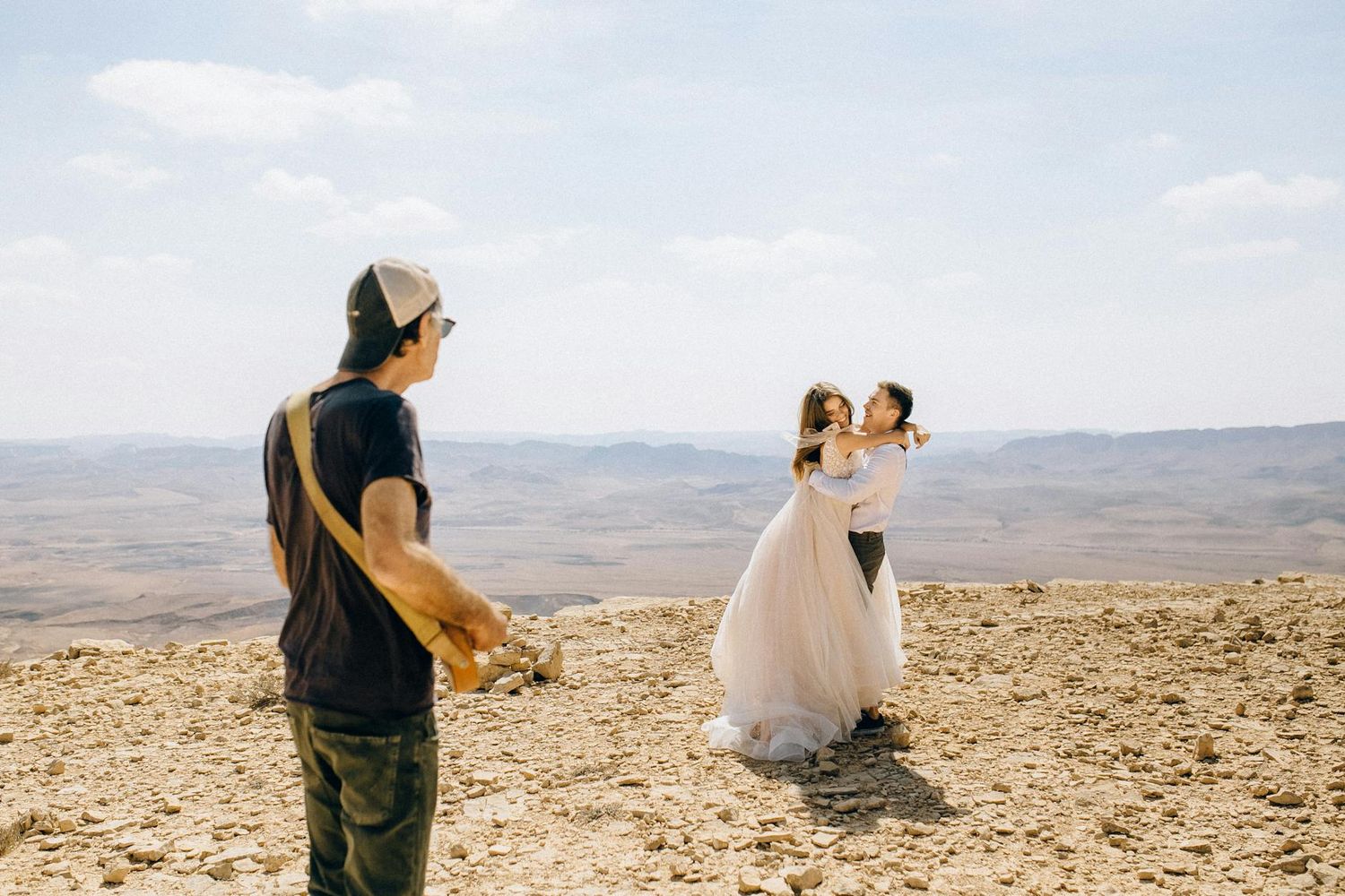 A photographer captures a wedding ceremony on a rocky desert overlook with vast mountains in the distance.