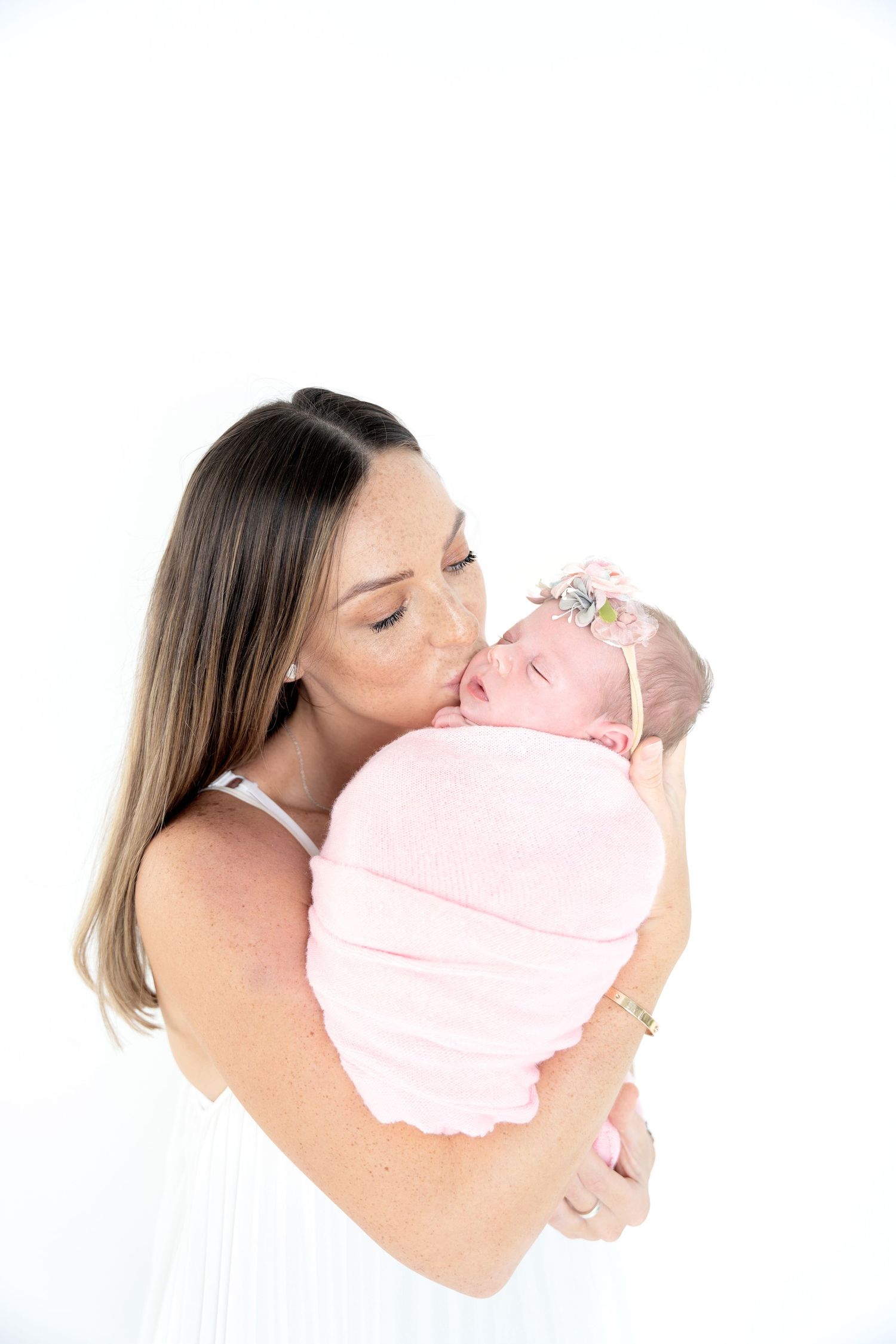 A tender moment between parent and swaddled infant in pink against a white background.