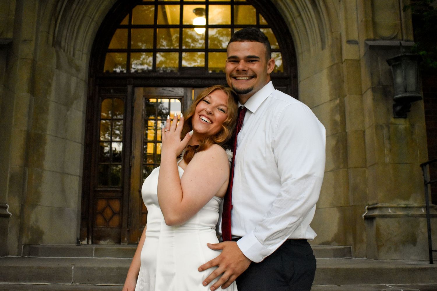 A romantic proposal moment on stone steps outside an ornate building with a man kneeling in a white shirt.