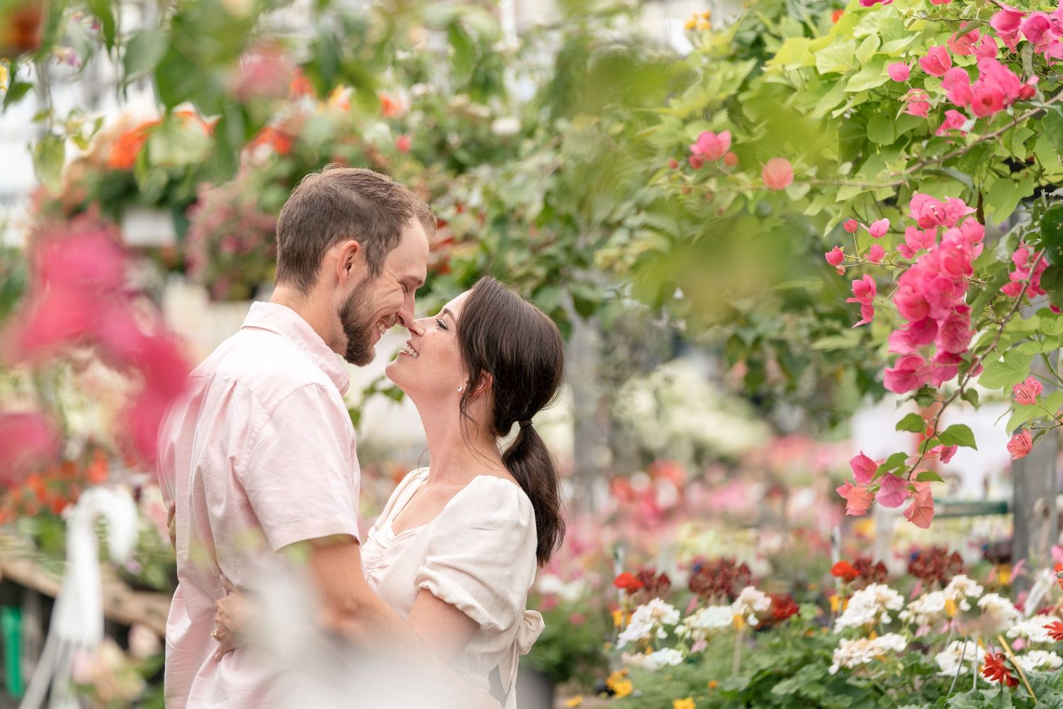 Wedding party members in formal black suits and blush pink dresses hold white floral bouquets while standing in a line outdoors.