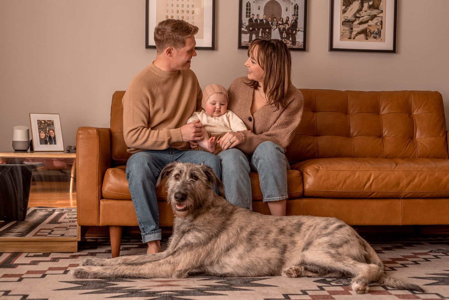 Cozy family scene on a brown leather couch with a large dog resting on a patterned rug.
