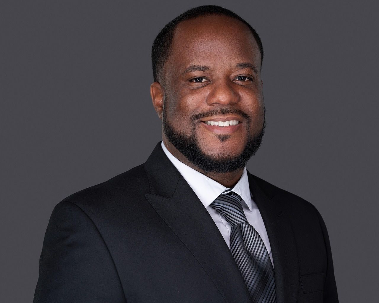 Professional headshots of business professionals against dark gray background wearing suits and smiling at camera.