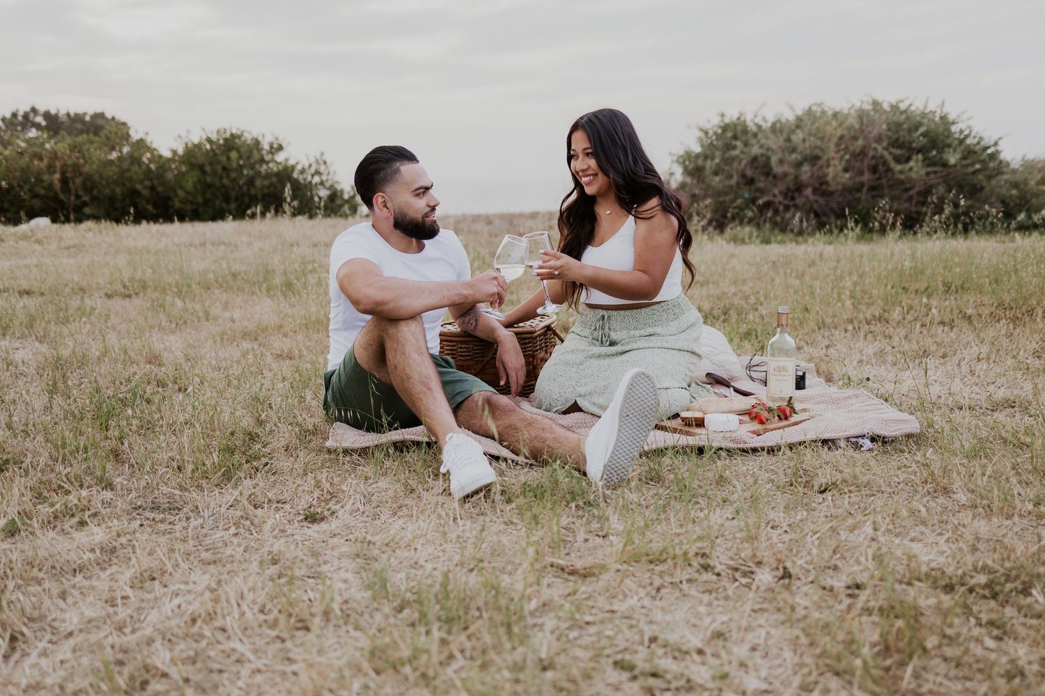 Couple enjoys intimate picnic on blanket in grassy field during golden hour.