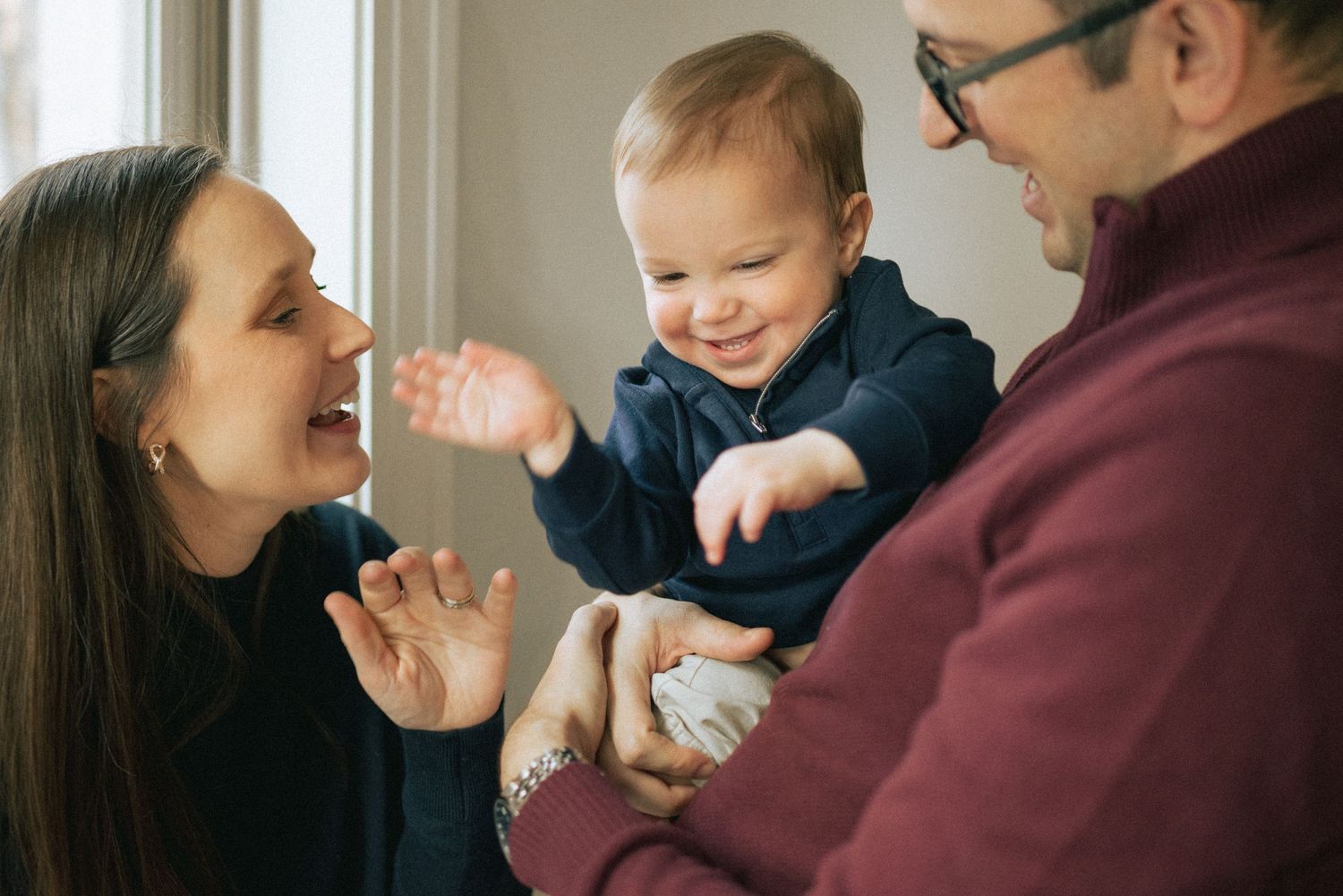 A happy family shares a joyful moment together, smiling and interacting warmly in natural window light.