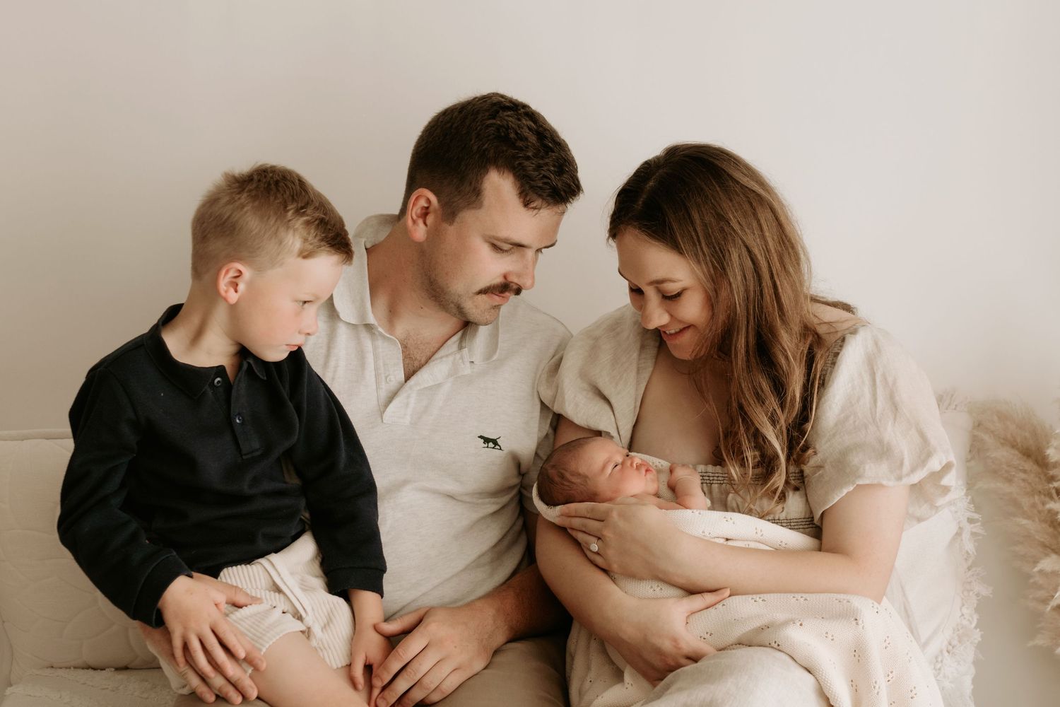 Family sitting together on couch with newborn and older child in neutral tones.
