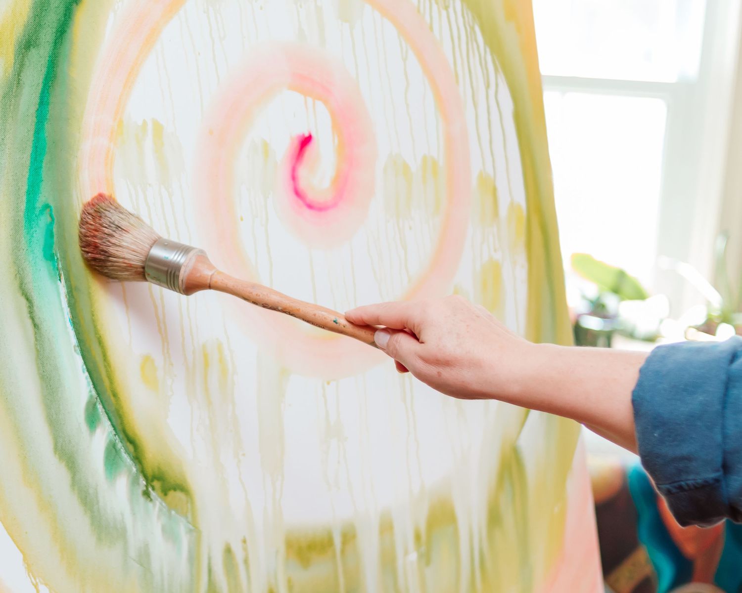 Hand holding paintbrush against colorful spiral watercolor painting.