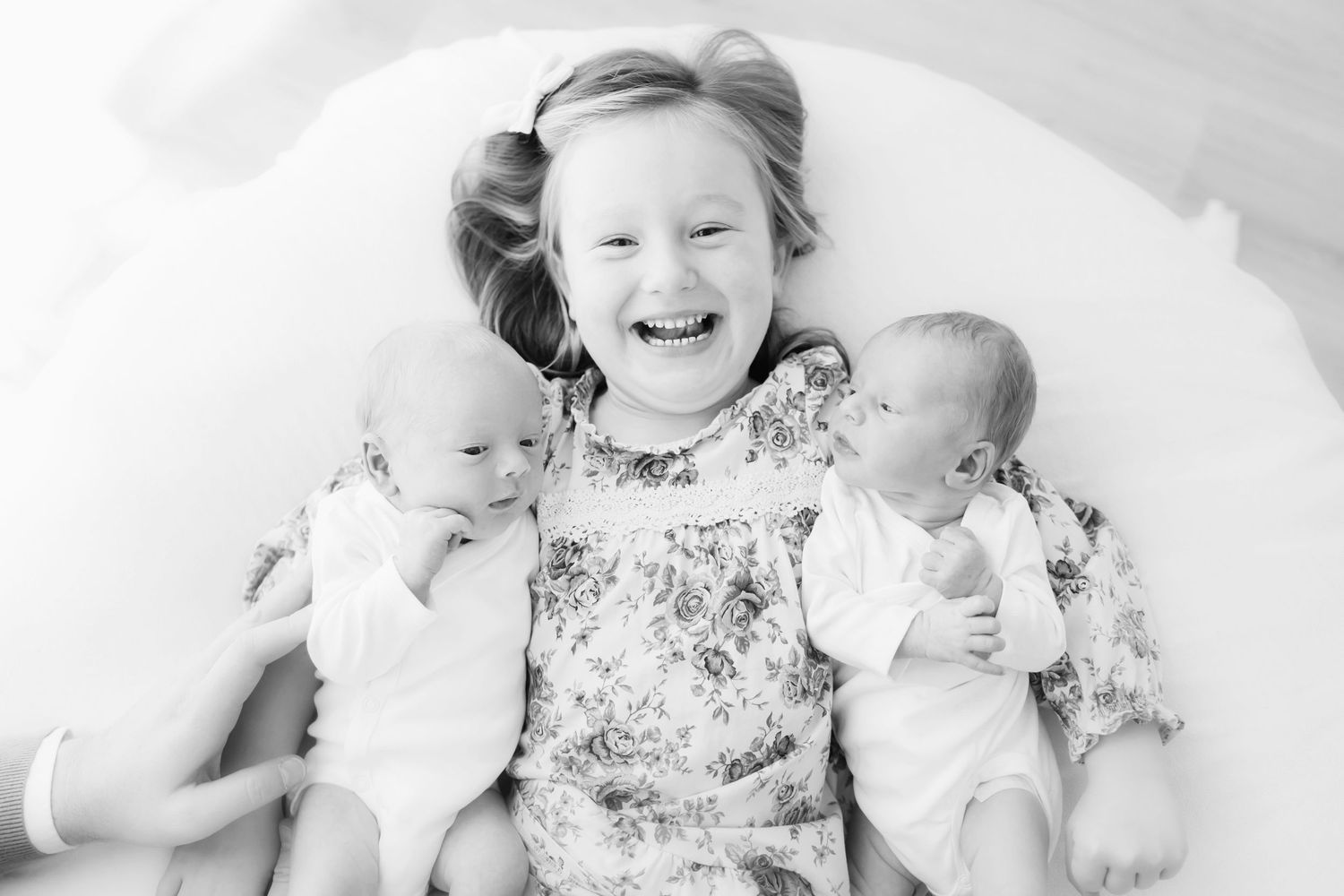 Happy family of four posing with newborn twins, parents smiling with toddler girl standing behind them.