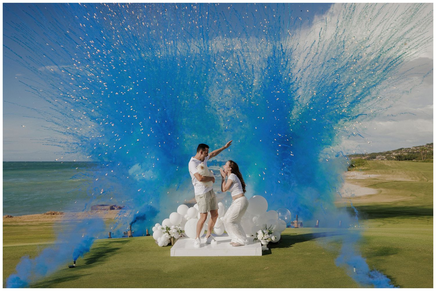 Gender reveal photoshoot at St. Regis Punta Mita, with a couple celebrating beneath blue and pink powder by the ocean.