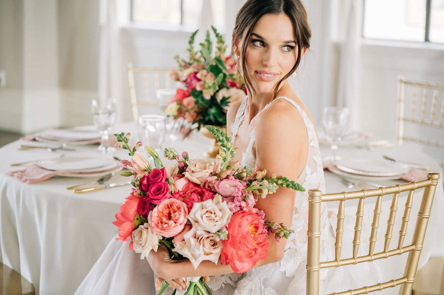 Elegant bride in off-shoulder white gown poses by large windows in dramatic black and white photo.