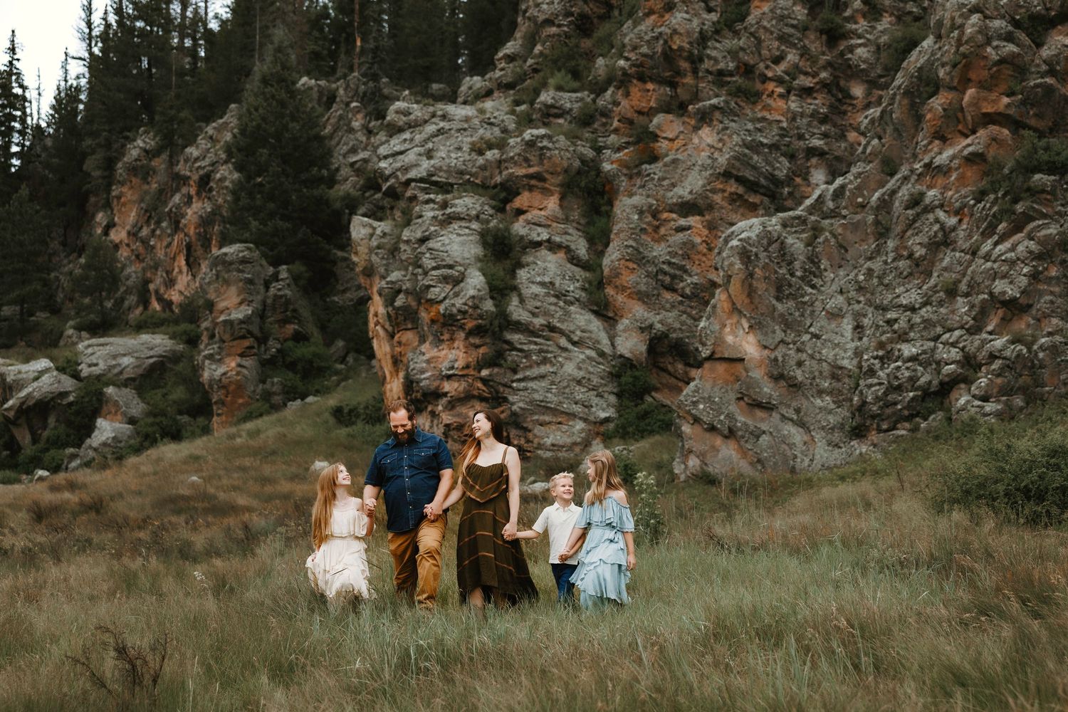 Family of six with young children poses in mountain meadow surrounded by pine trees and rocky cliffs.