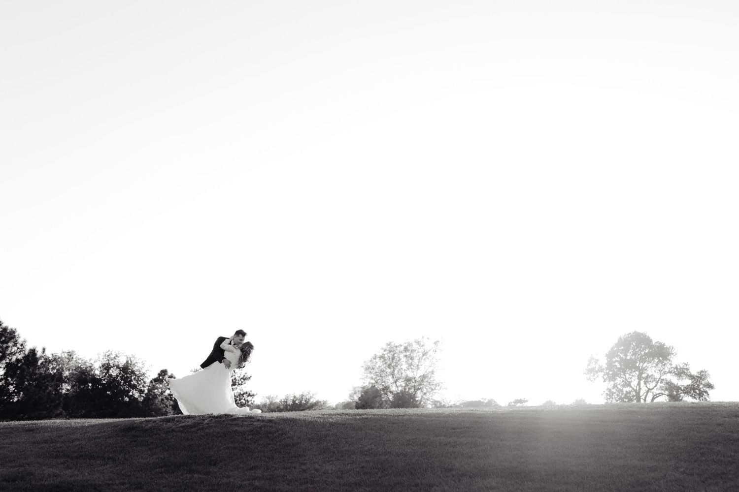 Bride and groom kissing on a horizon at sunset, captured in a clean, natural photography style, wedding photographer style in nebraska