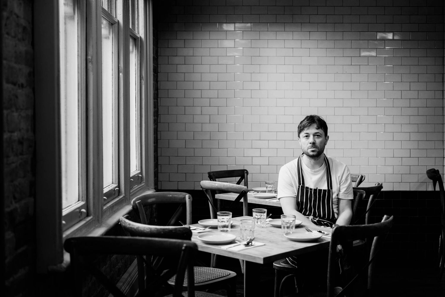 Chef leaning against colorful storefront window during daytime.