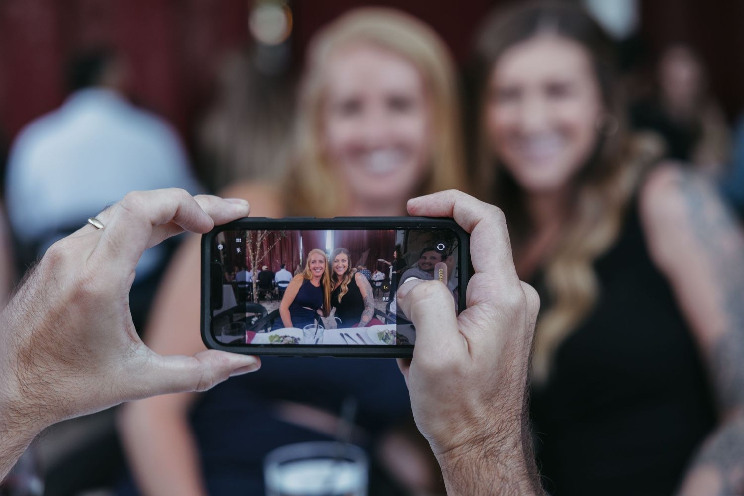 A person holding a smartphone taking photos of people in a crowd at a social gathering.