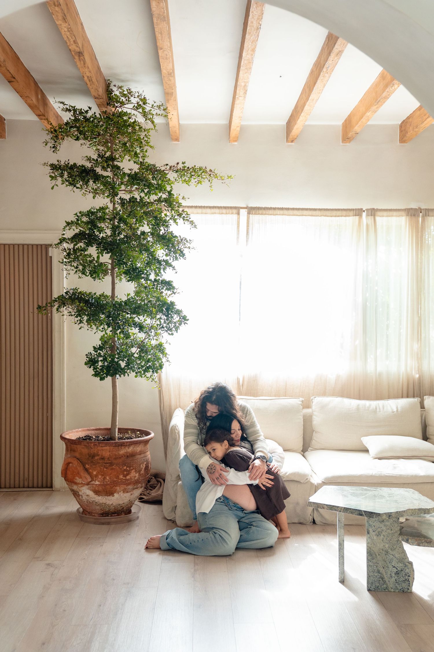 A sequence of photos showing a couple embracing and sitting together in a minimalist room with wooden beams and a potted tree.