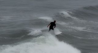 Silhouette of surfer riding large ocean wave in overcast conditions.