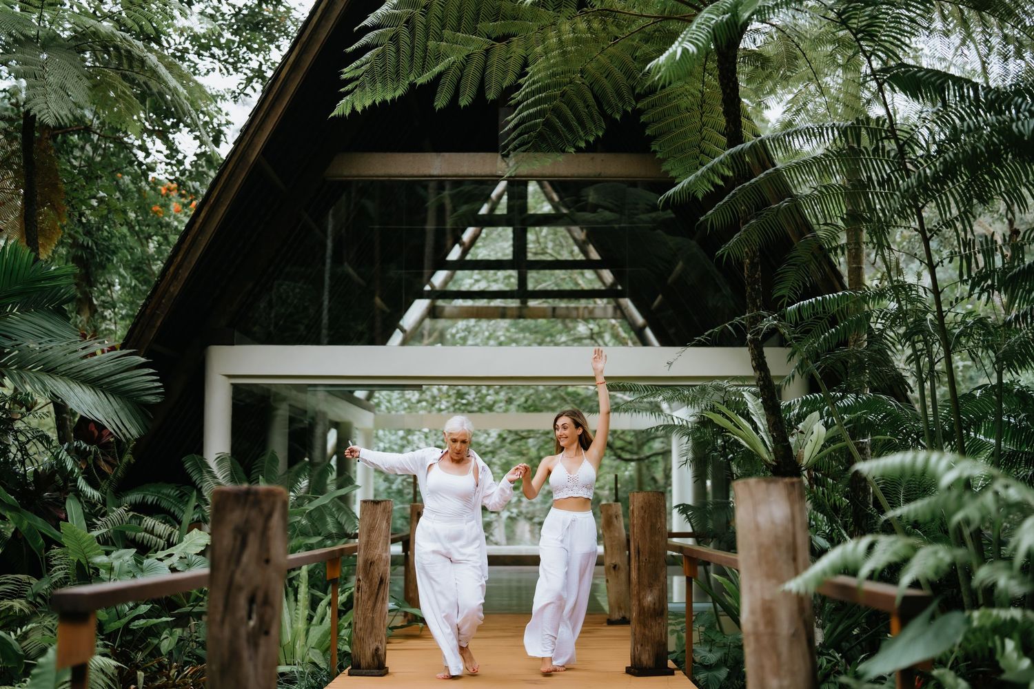 Two people in white outfits walk through tropical garden pathway with A-frame structure.