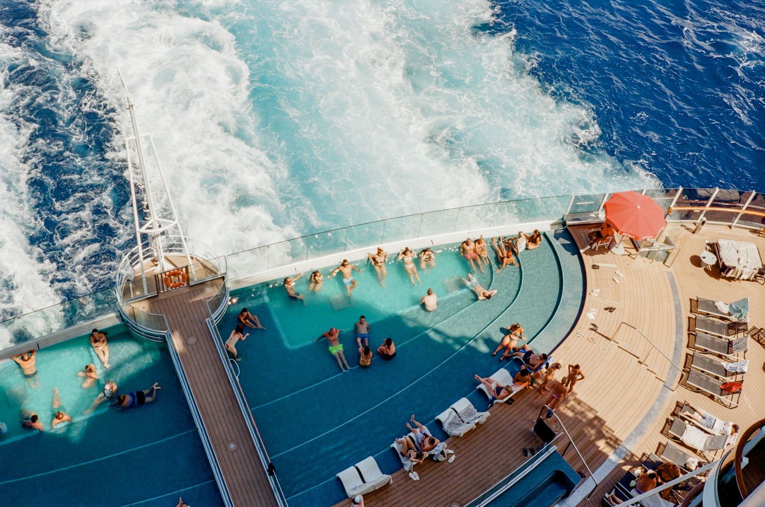 Aerial panoramic view of cruise ship deck with turquoise ocean waves crashing against the bow of the vessel.