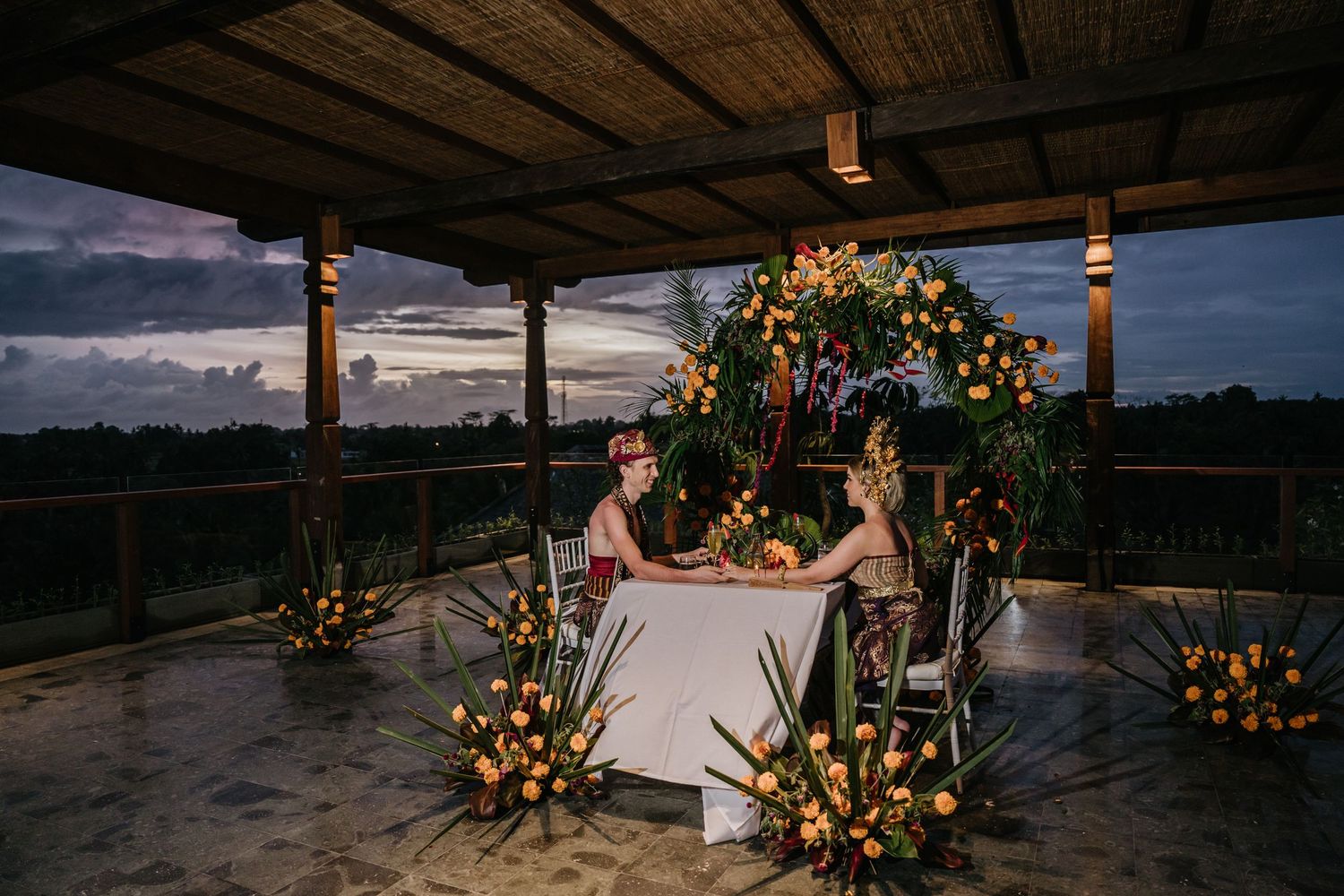 Rustic wooden deck wedding venue decorated with orange and pink flowers at sunset.