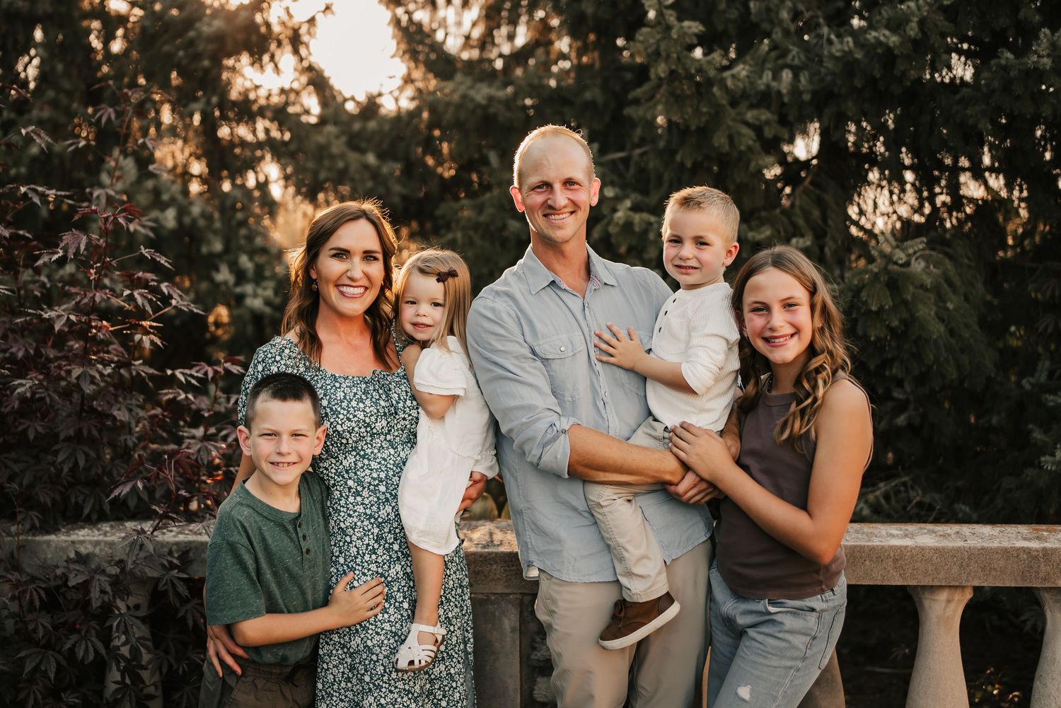 Family standing in front of fall trees at sunset during fun family photos.