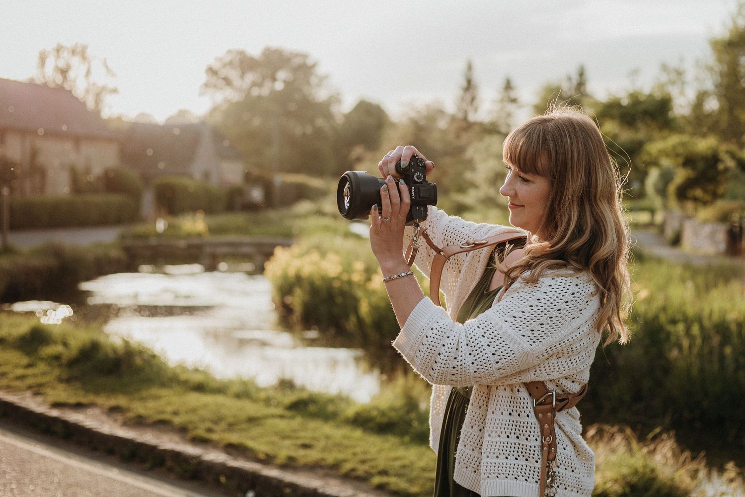 Person in white sweater taking photos near a scenic waterfront at sunset.