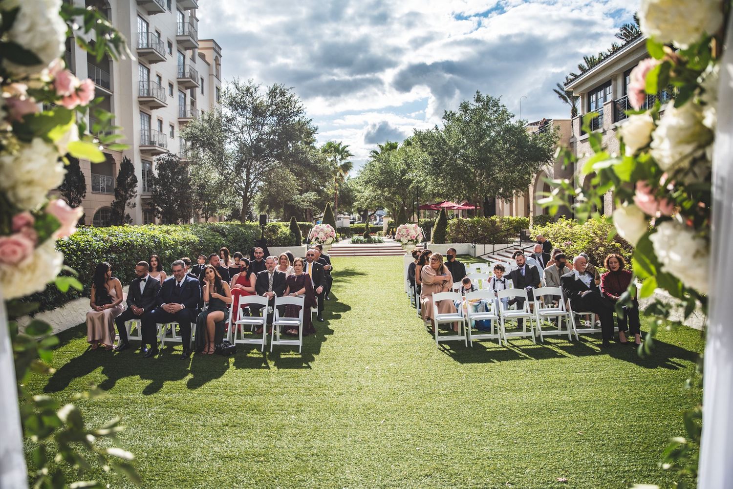 Outdoor wedding ceremony on green lawn with white chairs and floral arch at elegant venue. The Alfond Inn.