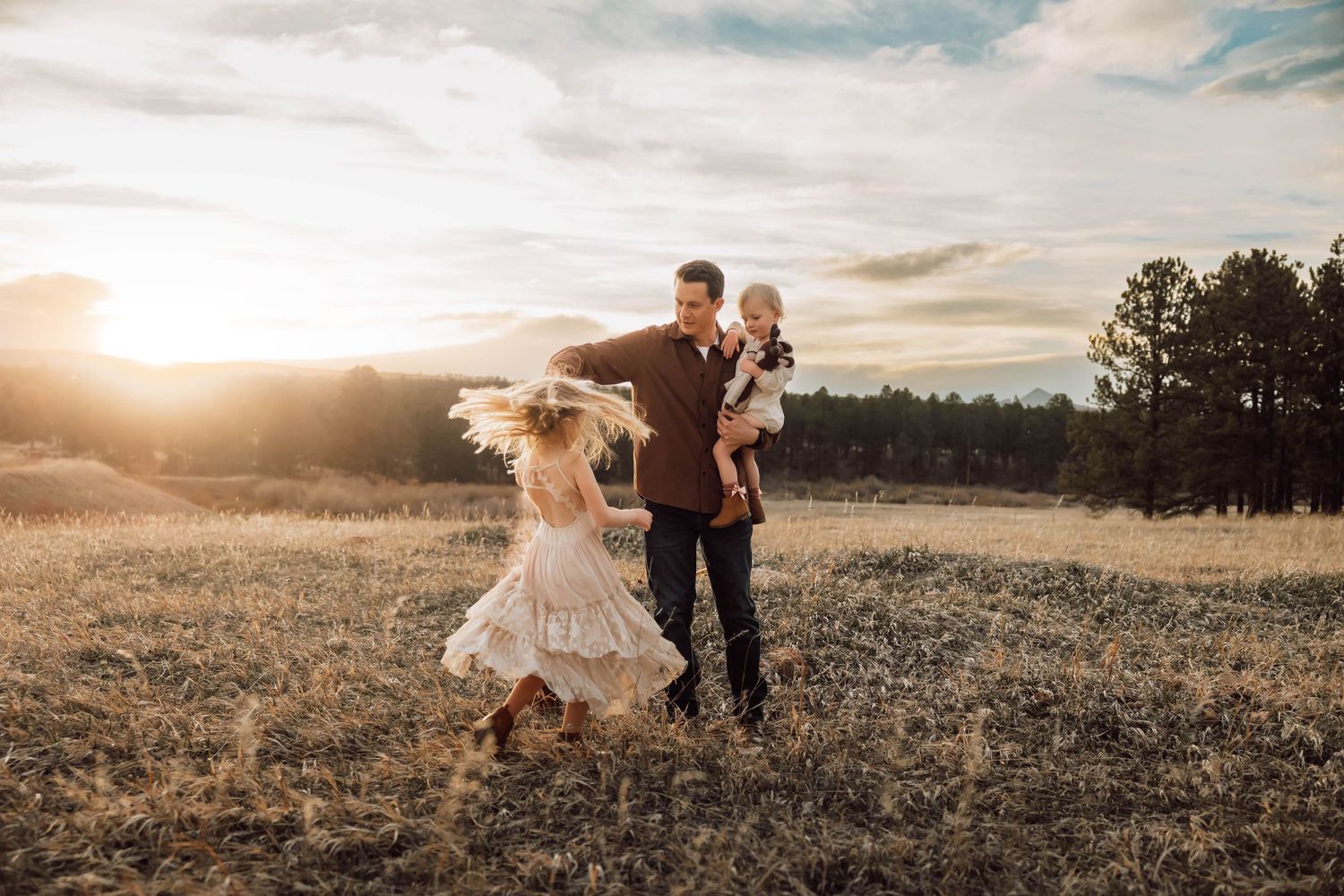 A family runs together through a golden field at sunset with mountains in the background.