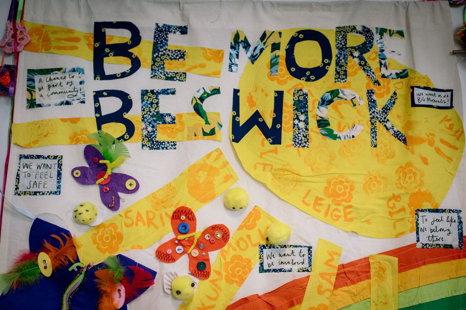 Colorful classroom bulletin board display with words 'Be More' decorated with student artwork and butterflies.
