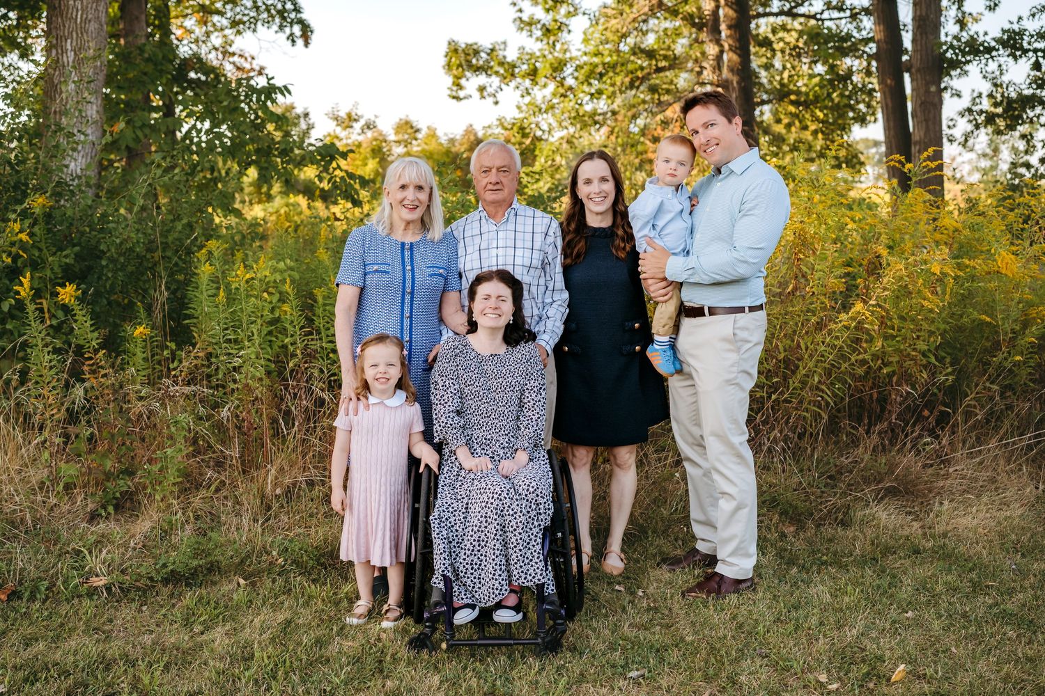 A family poses together outdoors in a natural setting during golden hour with fall foliage in the background.