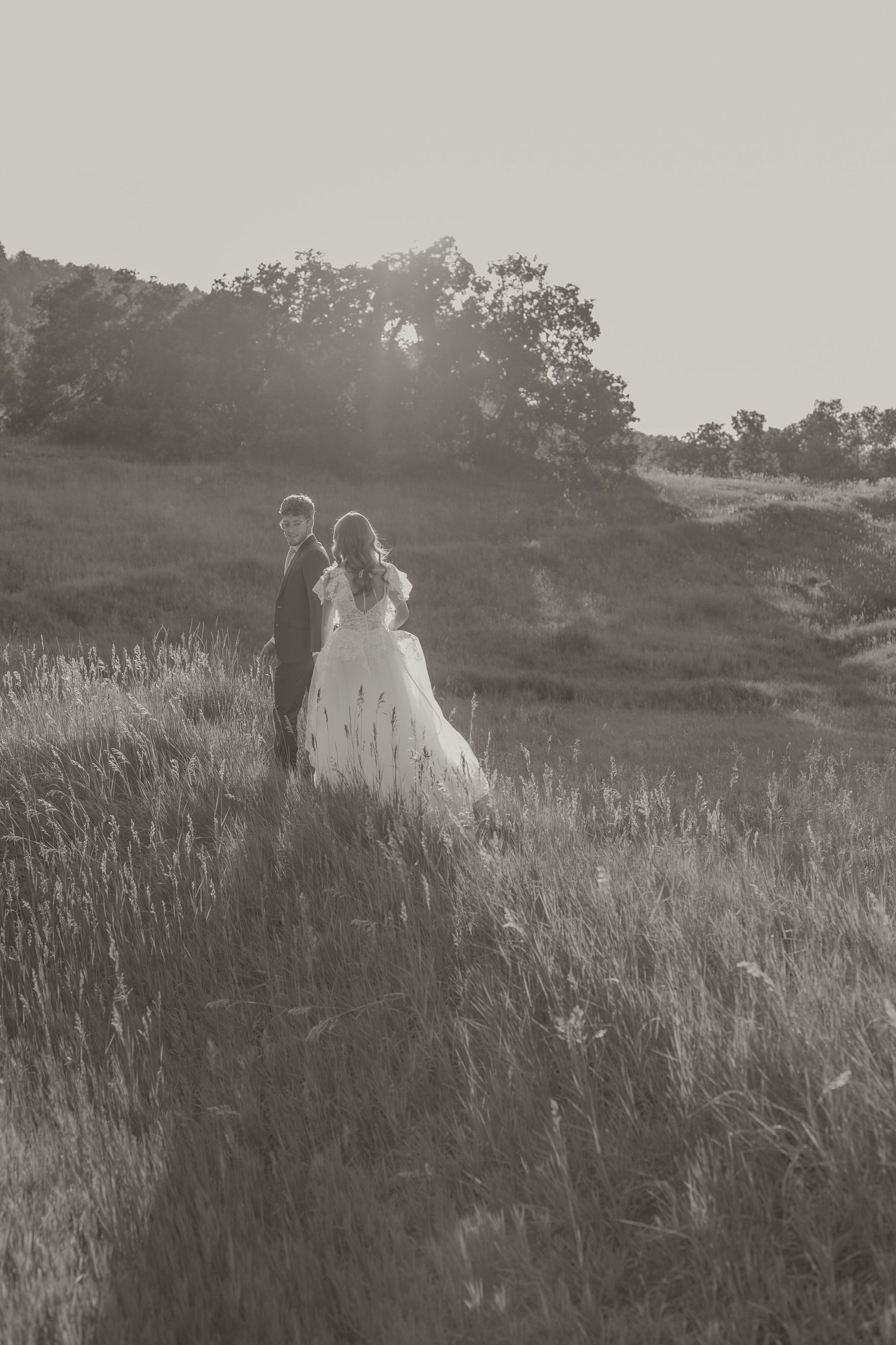 A couple in wedding attire share a playful kiss while holding a bouquet in a rustic outdoor setting.