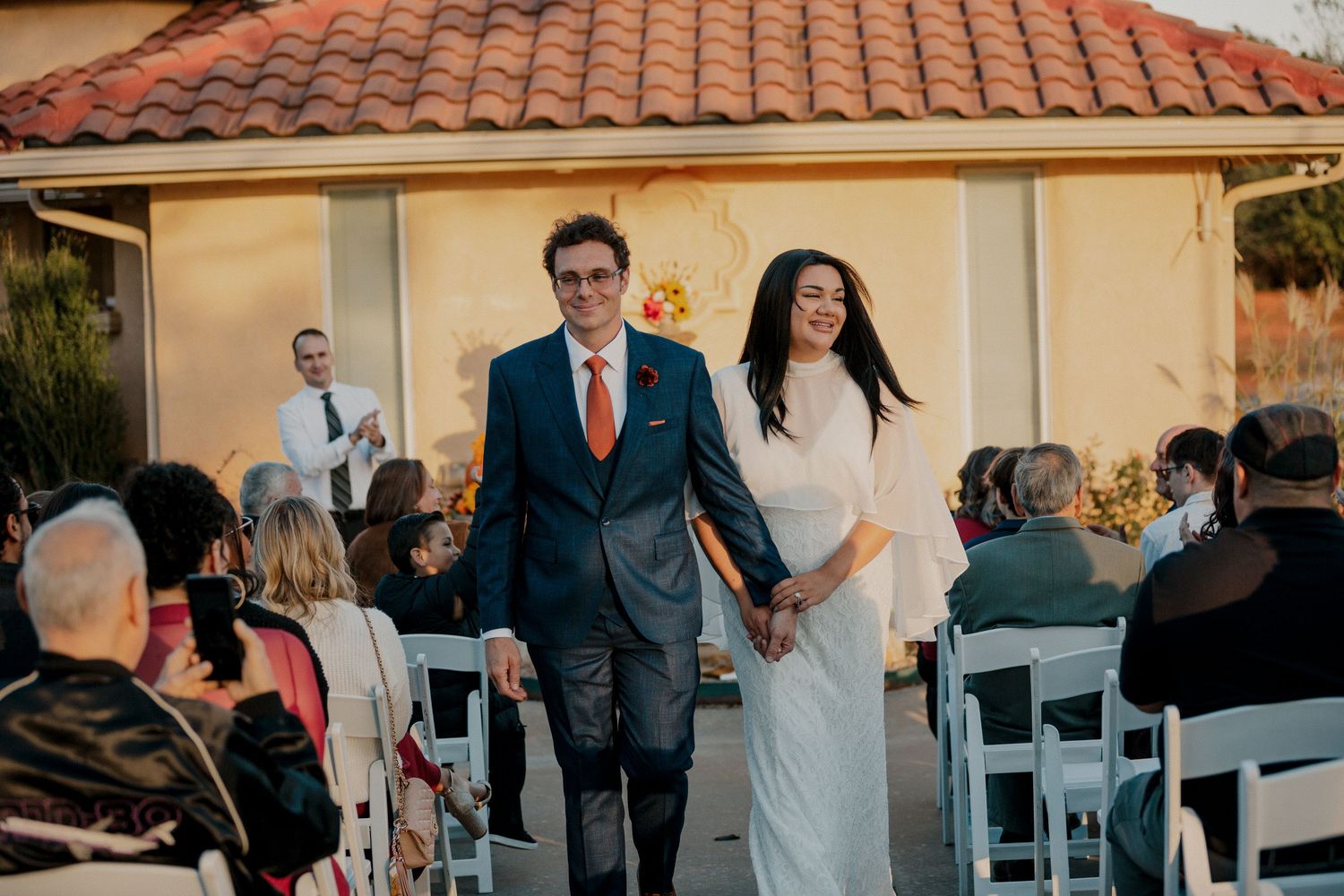 A newlywed couple walks hand in hand down the aisle after their outdoor wedding ceremony.