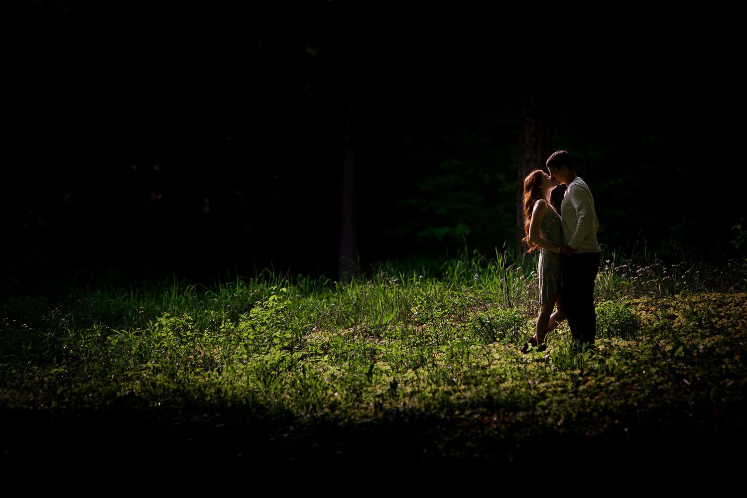A dark silhouette of a person walking in a grassy area illuminated by a spotlight at night.