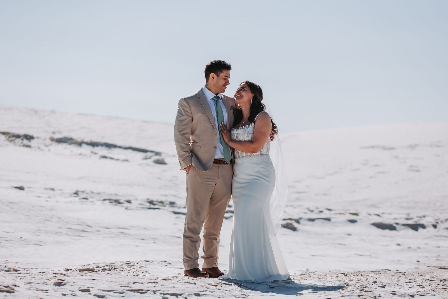 A couple in wedding attire embrace while standing on a snow-covered winter landscape.