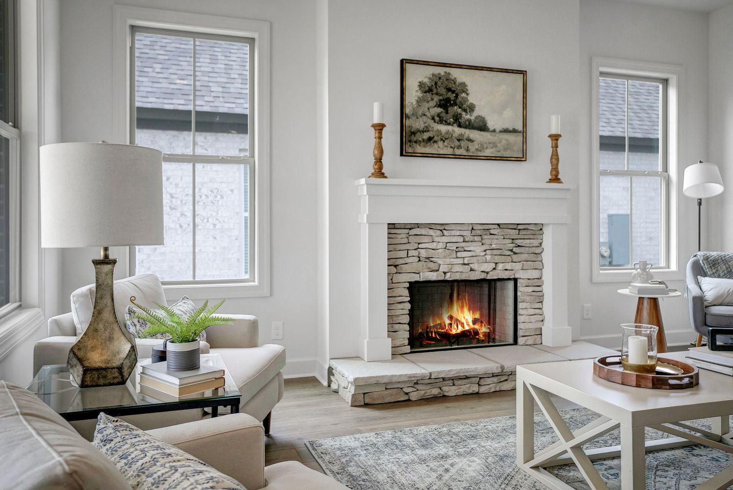 Modern living room features stone fireplace, white walls, and large windows overlooking natural scenery.