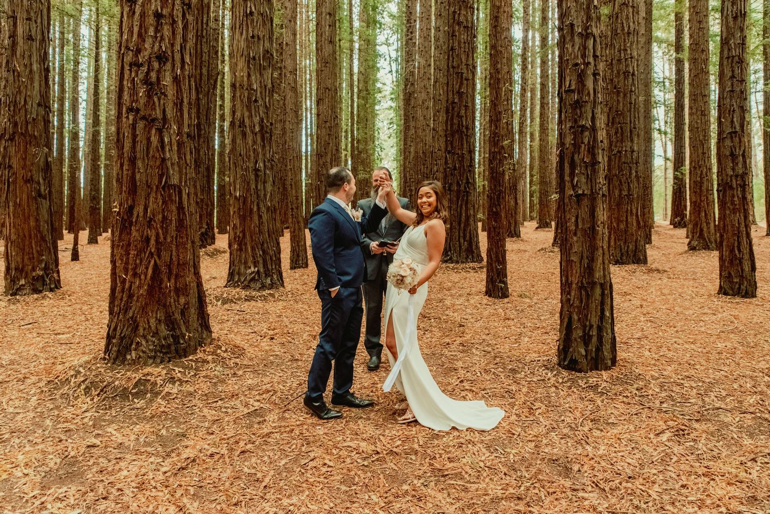 A romantic wedding ceremony takes place in a serene redwood forest with tall trees creating a natural cathedral.