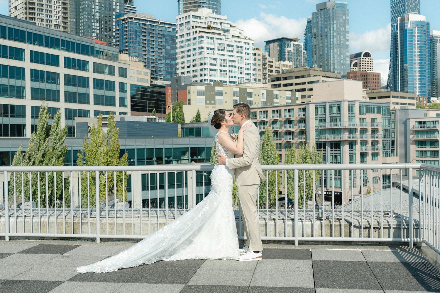 Bride and groom kissing on a rooftop terrace with Seattle city skyline in the background on their wedding day.