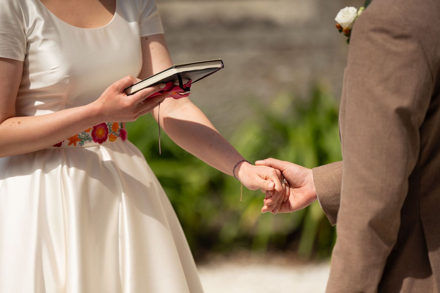 La mariée lit des vœux dans un livre pendant que le marié lui tient la main lors d'une cérémonie de mariage en plein air.