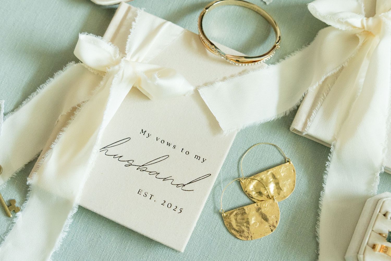 Elegant wedding flat lay with HER and HIS vows cards, gold bangles, Dior perfume, red floral fabric, and embroidered shoes.